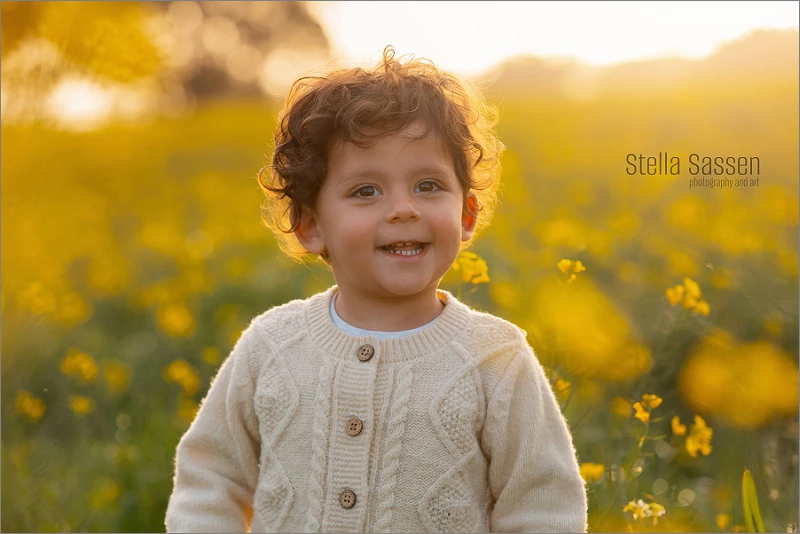 little boy laughing in a field of canola flowers at sunset